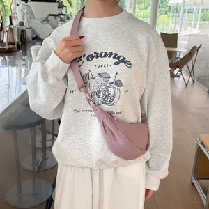 Detail view of the pink crescent crossbody bag worn by a model in a bright cafe setting