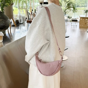 Detail of a pink-purple nylon half-moon crossbody bag shown on a model in a cafe