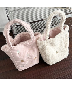 Detailed view of plush tote bags in pink and beige with Christmas embroidery and metal tag