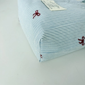 Gros plan du sac en toile à rayures bleues avec nœud rouge brodé et étiquette décorative