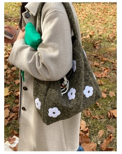 Detail of green plush tote bag with white flower embroidery on warm autumn lawn