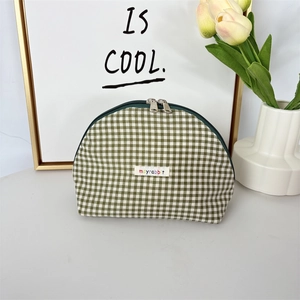 Detail of green gingham shell makeup bag with dual silver zippers and logo label