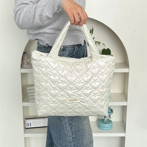 Detail view of a white quilted tote bag featuring heart pattern and soft padded handles