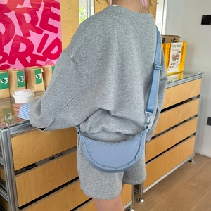 Blue nylon crescent bag with adjustable wide strap worn by model in a modern café