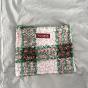 Close-up of pink and green plaid plush scarf with a leather logo patch on fuzzy wool fabric