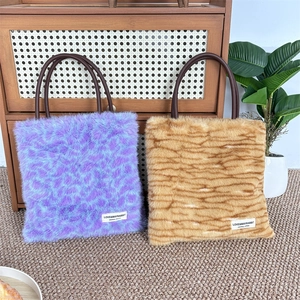 Winter faux fur tote bags with purple leopard and brown tiger prints on wooden background