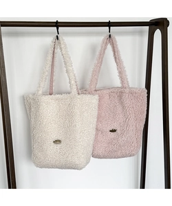 Detail of soft plush tote bags in beige and pink with oval metal brand plates