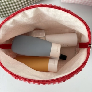 Close-up of red checkered makeup bag showing internal storage capacity with travel bottles