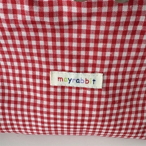 Close-up of red gingham fabric texture and stitched mayrabbit label on cosmetic bag