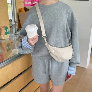 Fashionable beige nylon dumpling bag with adjustable strap worn over grey sportswear outfit