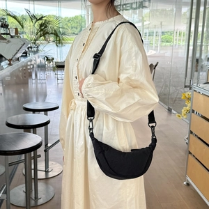 Close-up of a black crescent crossbody bag worn with a stylish beige pleated dress