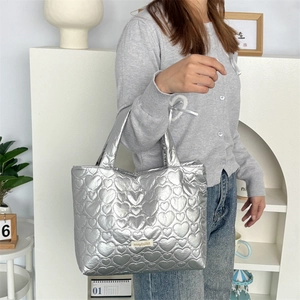 Detail of silver heart-quilted PU tote bag with a metallic finish and brand label