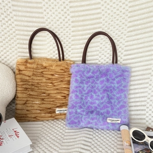 Detail of plush faux fur tote bags with leopard prints and leather handles on knit fabric
