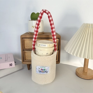 Detail of plush sherpa water bottle sleeve with red gingham handle on a cozy table