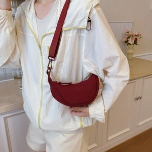 Detail of burgundy crescent crossbody bag showing wide strap and nylon texture on model