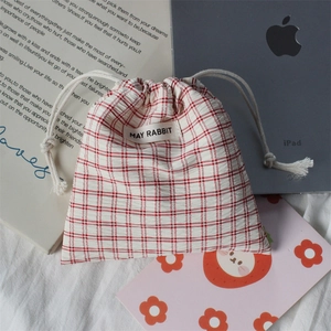 Detailed view of red plaid drawstring fabric bag with white brand label on a cozy desk