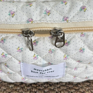 Détail des fermetures éclair et de l'étiquette sur une trousse de maquillage matelassée fleurie