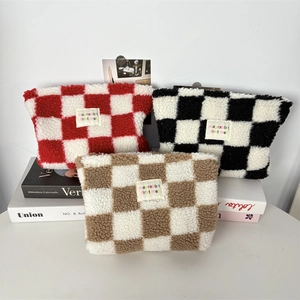 Close-up of plush checkered makeup bags in red, black, and brown with woven labels