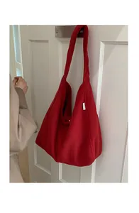 Detail of red wool tote bag showing fuzzy texture and side woven label on a door