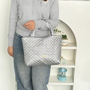 Detailed close-up of woven metallic silver tote bag with gold logo plaque on side