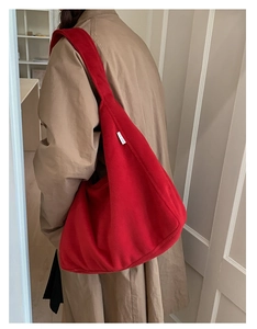 Detail of red wool tote bag with white woven label on model in cozy indoor setting