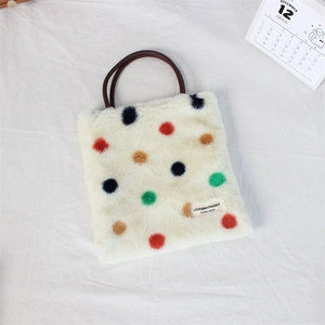 Flat lay of a plush cream tote bag with colorful polka dots on white textured fabric