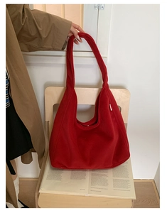 Large red plush hobo bag placed on a wooden chair with a magazine for autumn vibes