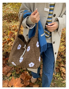 Detail of a brown plush tote bag with white floral embroidery and wooden button closure