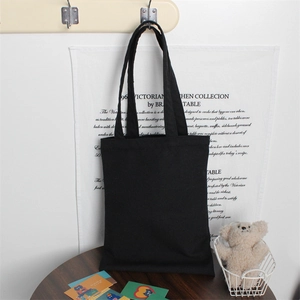 Detailed view of the thick black cotton canvas tote bag hanging on a hook in a cozy setting