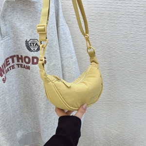 Detail showing light yellow crescent crossbody bag with adjustable strap in hand