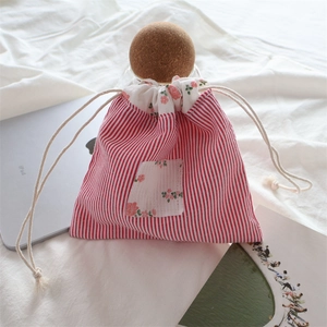 Détail de la pochette en coton à rayures rouges et poche fleurie sur literie blanche