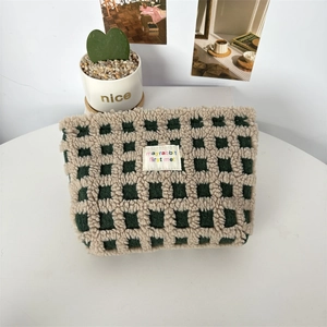 Detail of green and beige checkered plush makeup bag with woven brand label on white desk