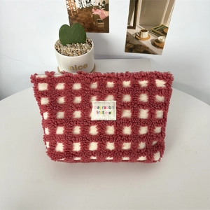 Close-up of red plaid plush cosmetic bag with 'mayrabbit' logo on a white desk