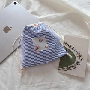 Gros plan d'une pochette à cordon rayée bleue avec écusson fleuri sur un fond en tissu
