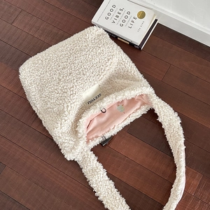 White faux shearling tote bag with SEEYOU label shown on dark wooden floor background