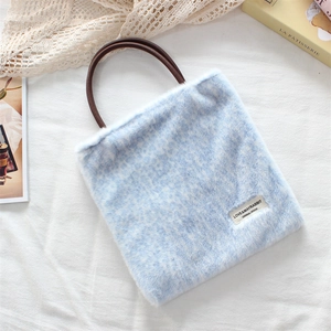 Detailed view of light blue plush handbag with brown handles on white fabric