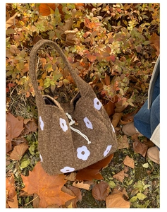 Detail of plush brown tote bag with white flower embroidery against autumn leaves