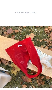Detail shot of red knit tote bag with white bird embroidery in a warm autumn setting