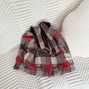 Detail of plaid tote bag featuring red and green patchwork fabric on a textured sofa