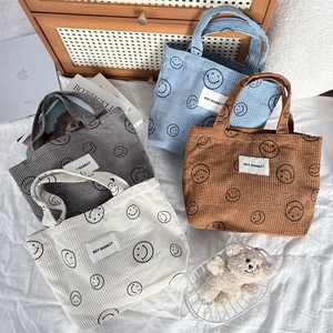 Close-up of corduroy tote bags in four colors with smiley patterns and logo detail