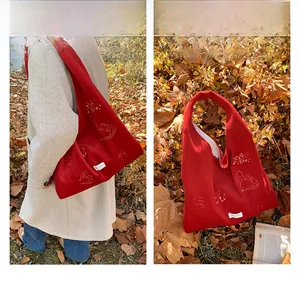 Detail of red embroidered tote bag with bird patterns on thick wool fabric shown outdoors