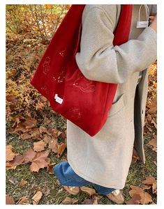 Detailed embroidery of birds and houses on a red hobo tote bag in an autumn outdoor scene
