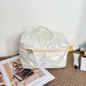 Detail of off-white quilted cosmetic bag with bow patterns and sturdy handle