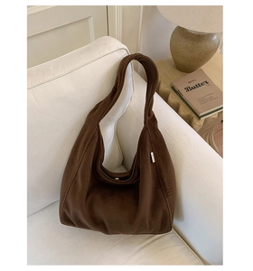 Detail of a dark brown suede hobo bag placed on a white sofa in a cozy interior setting