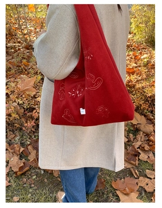 Detail of red suede tote bag with white bird embroidery shown on a model's shoulder