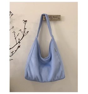 Detail of light blue fuzzy fleece tote bag hanging on a hook in a minimalist setting