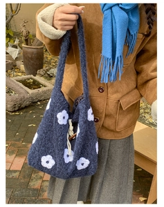 Detail of navy knit tote bag featuring large white floral embroidery and horn buckle