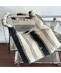 Dettaglio della borsa tote in peluche a righe bianche e nere con emblema in oro e tracolla arricciata