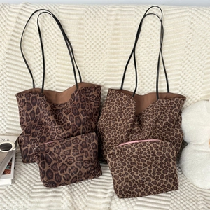 Set of two leopard print faux suede tote bags with slim leather straps on white knit surface