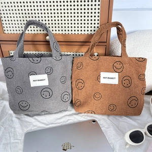 Detail of gray and brown corduroy tote bags with smiley prints and woven brand labels